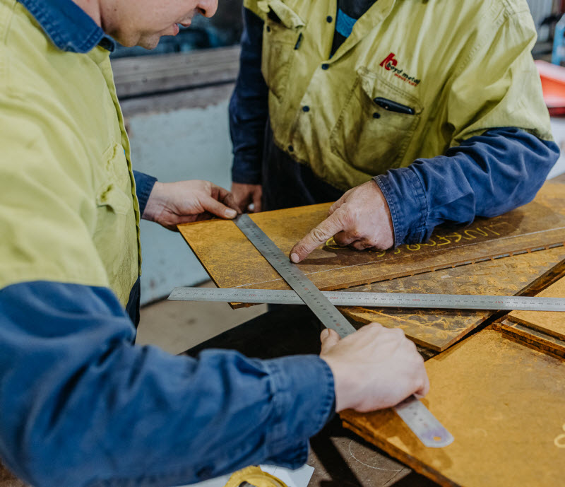 Workers measuring a steel sheet